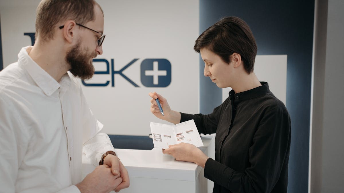 Customer discussing information sheet with receptionist in clinic.
