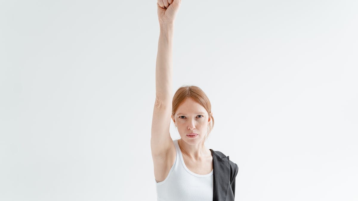 A woman in a white tank top raises her fist in a powerful gesture of strength and equality.
